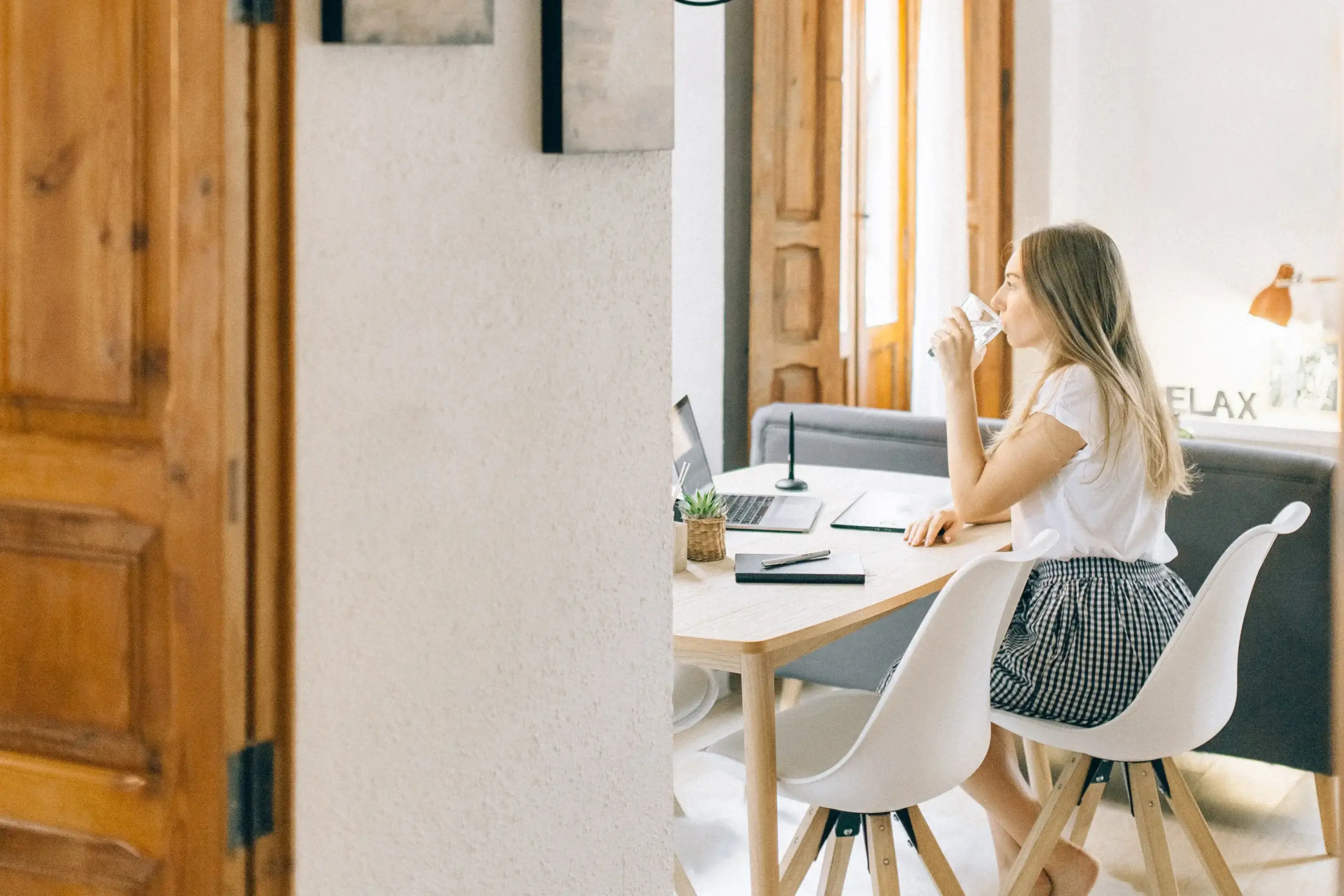 woman sitting at a table with her laptop and notepad while drinking water